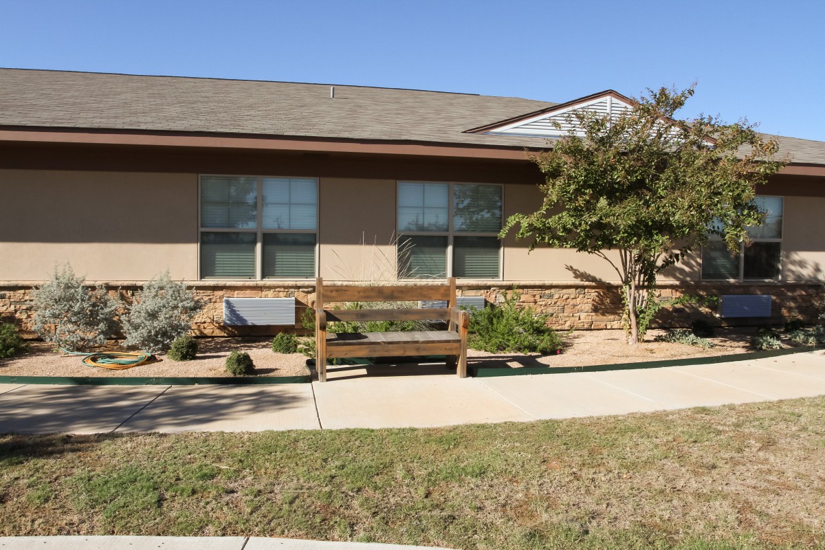 A small house with a bench in front and landscaped garden.