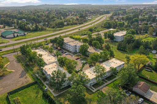Aerial view of a residential apartment complex surrounded by lush greenery and adjacent to a highway.
