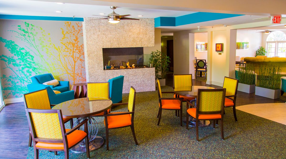 A modern and colorful seating area featuring tables, vibrant chairs, and a fireplace.
