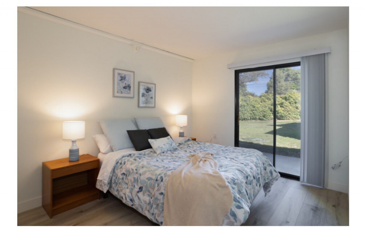A cozy bedroom with a large bed, bedside lamps, and a sliding glass door offering a view of the greenery outside.