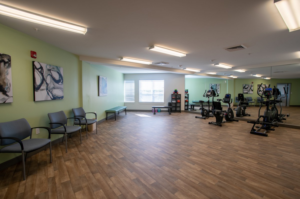 An empty fitness center with exercise equipment and wooden flooring.