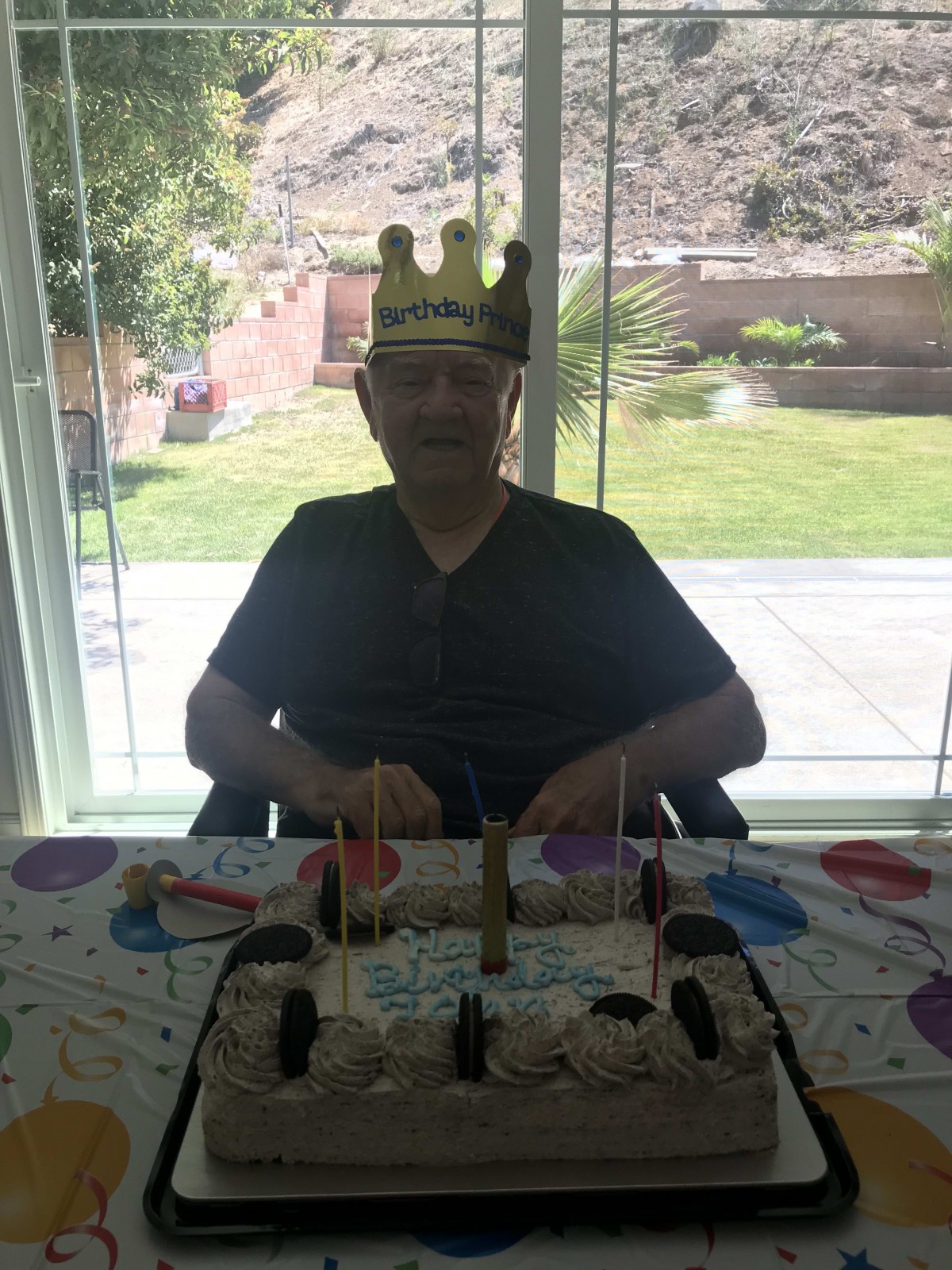A person wearing a festive crown sits at a table with a birthday cake.