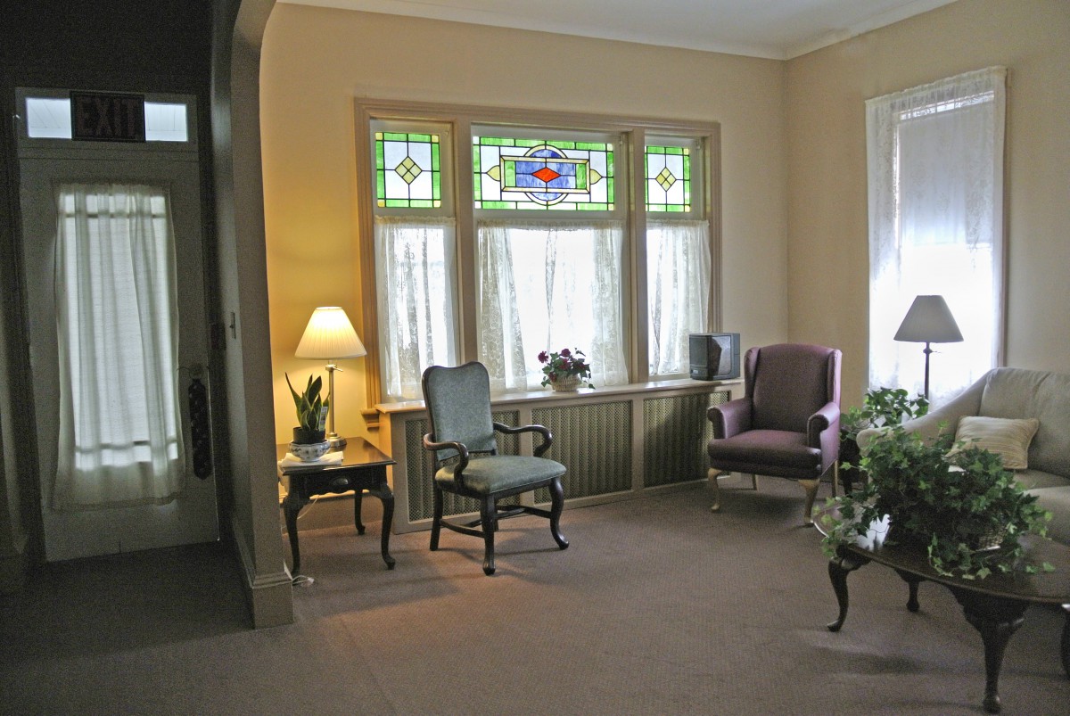 A cozy living room with stained glass windows, featuring armchairs and a side table with a lamp.