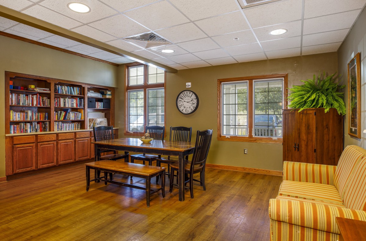 A well-lit conference room featuring a wooden table with chairs, bookshelves, and large windows.