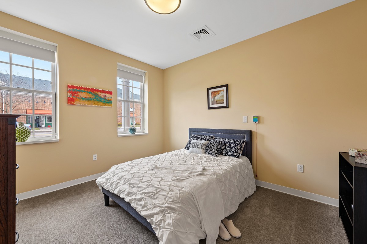 A tidy bedroom featuring a bed with patterned pillows, wall art, and a window with natural light.