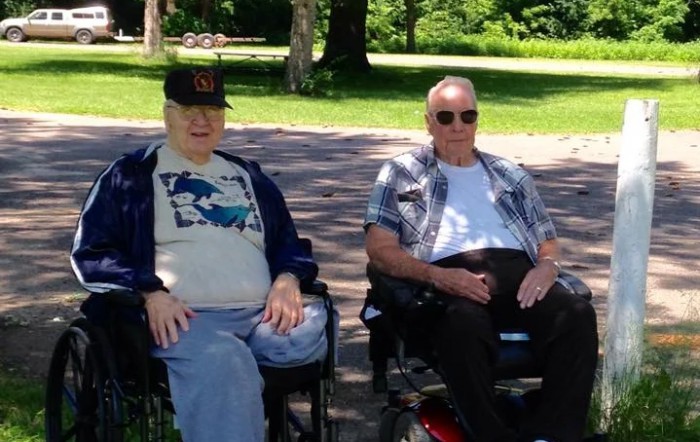 Two men sitting in wheelchairs enjoying a sunny day in the park.