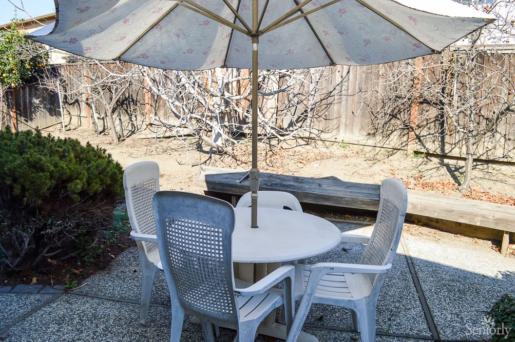 A patio set in a backyard, featuring a round table with four chairs and an umbrella.