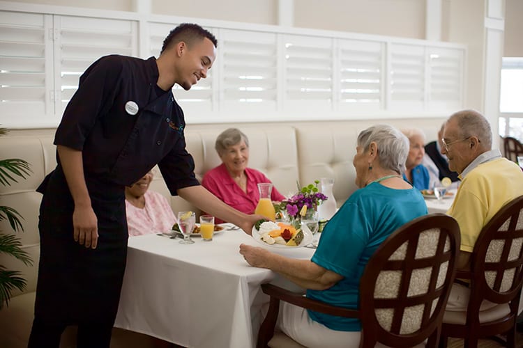 A waiter serving food to elderly patrons at a dining table.
