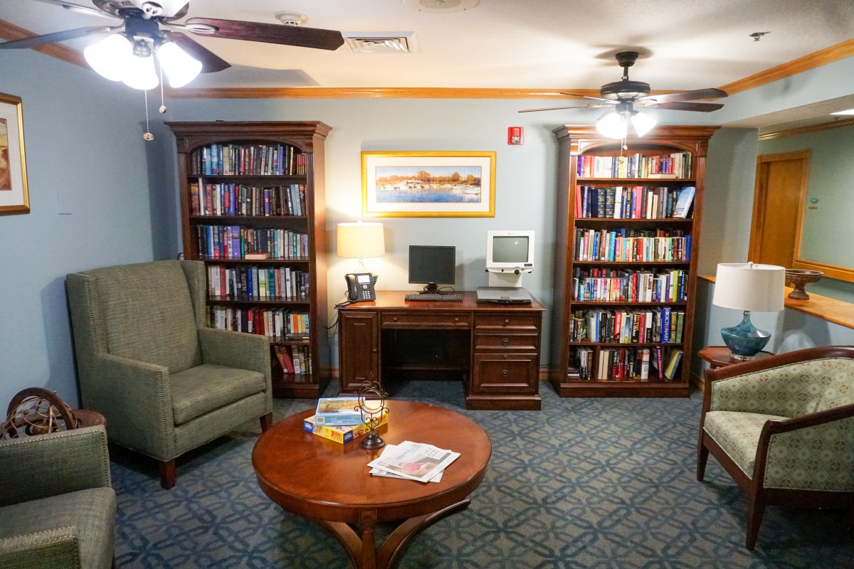 A cozy library reading area featuring bookshelves, a computer desk, armchair, and coffee table.