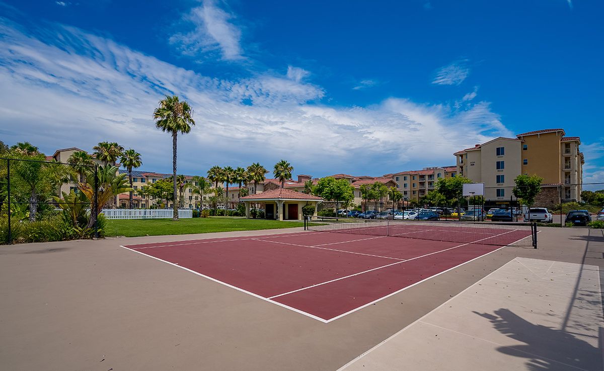 A sunny day at a residential complex with a tennis court and palm trees.