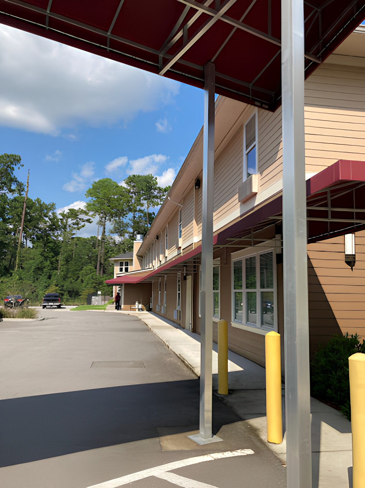 A view of a building with an awning and a nearby parking lot on a sunny day.