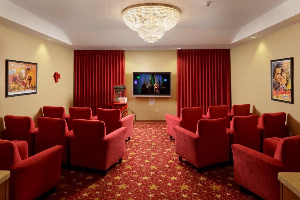 A cozy home theater with red upholstered chairs, a large screen, and elegant lighting.
