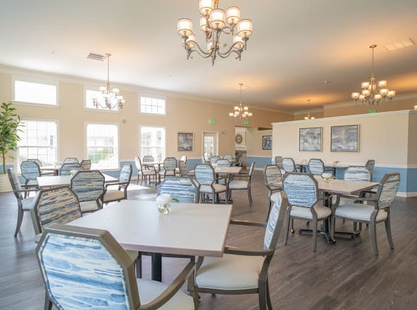 A spacious dining hall with elegant chandeliers, neatly arranged tables and chairs.