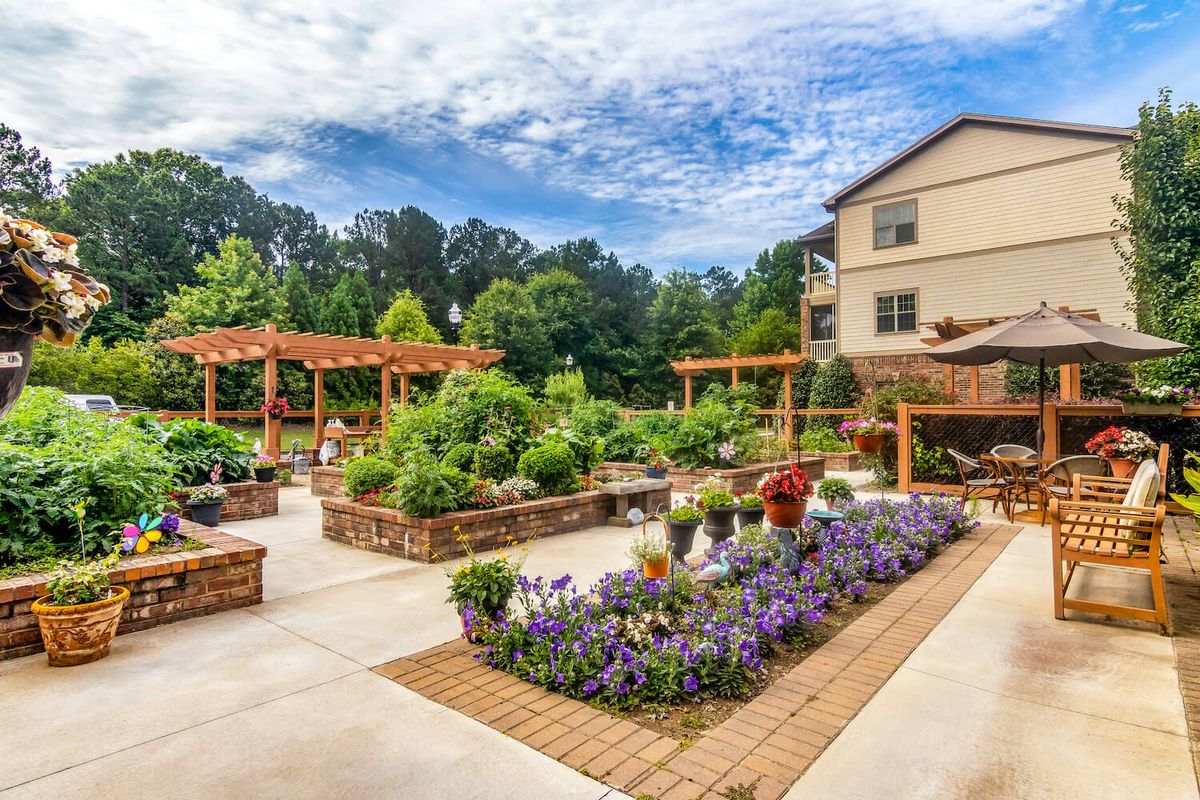 A beautifully landscaped garden with various blooming flowers and plants, adjacent to a building on a sunny day.