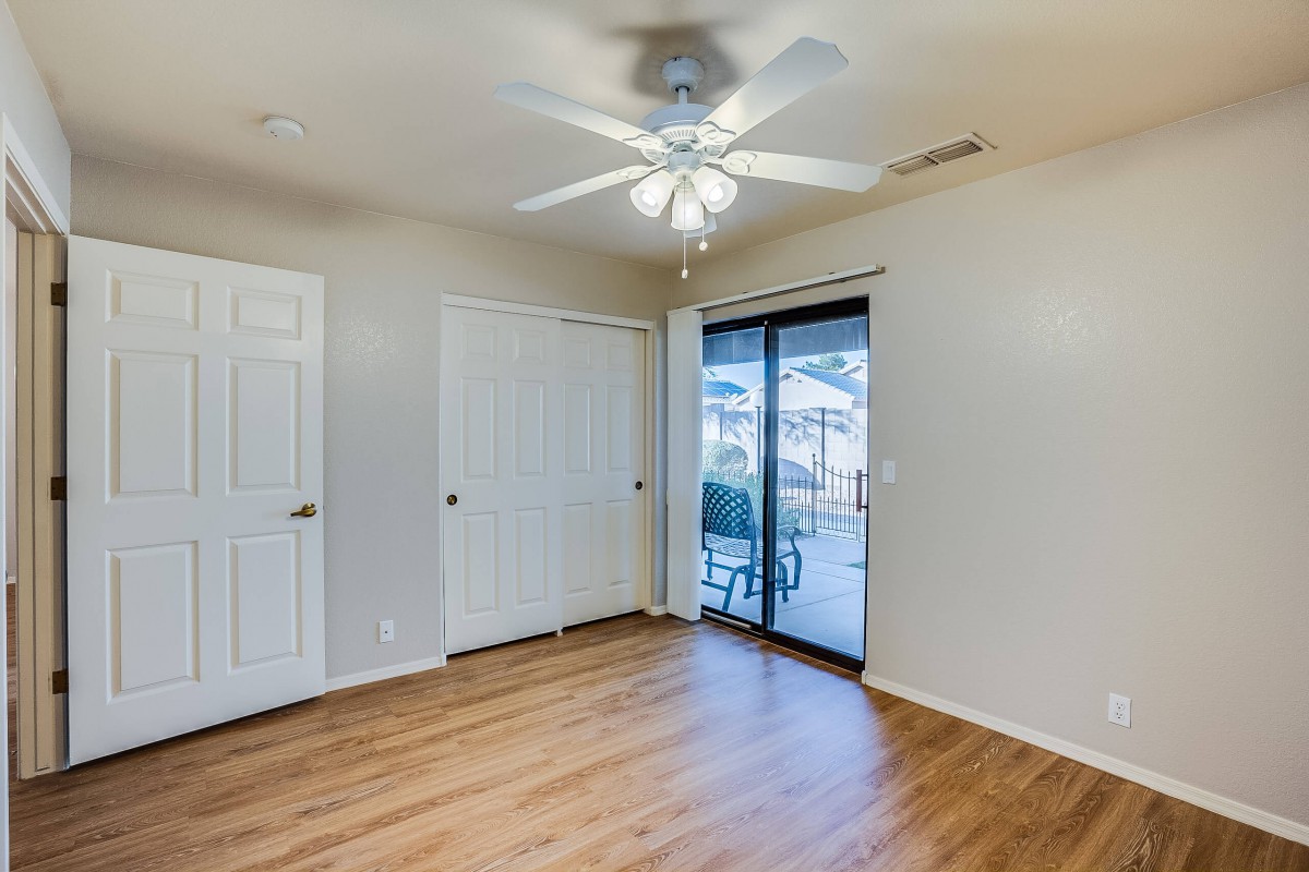 An empty room with wood flooring, a ceiling fan, and sliding glass doors leading outside.