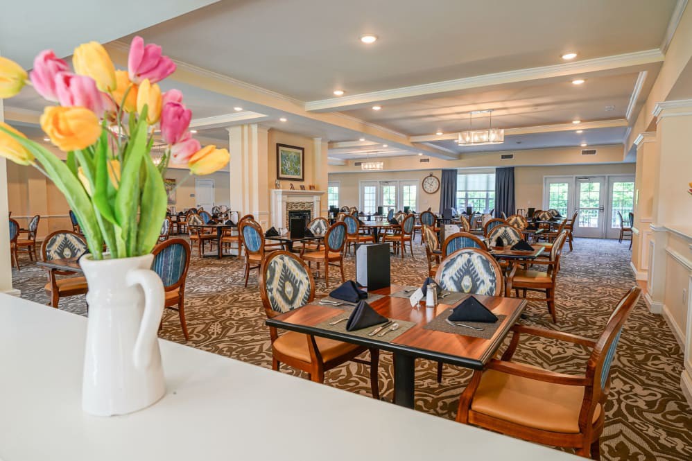 A well-decorated restaurant dining area with neatly arranged tables and chairs, featuring a vase of colorful flowers.