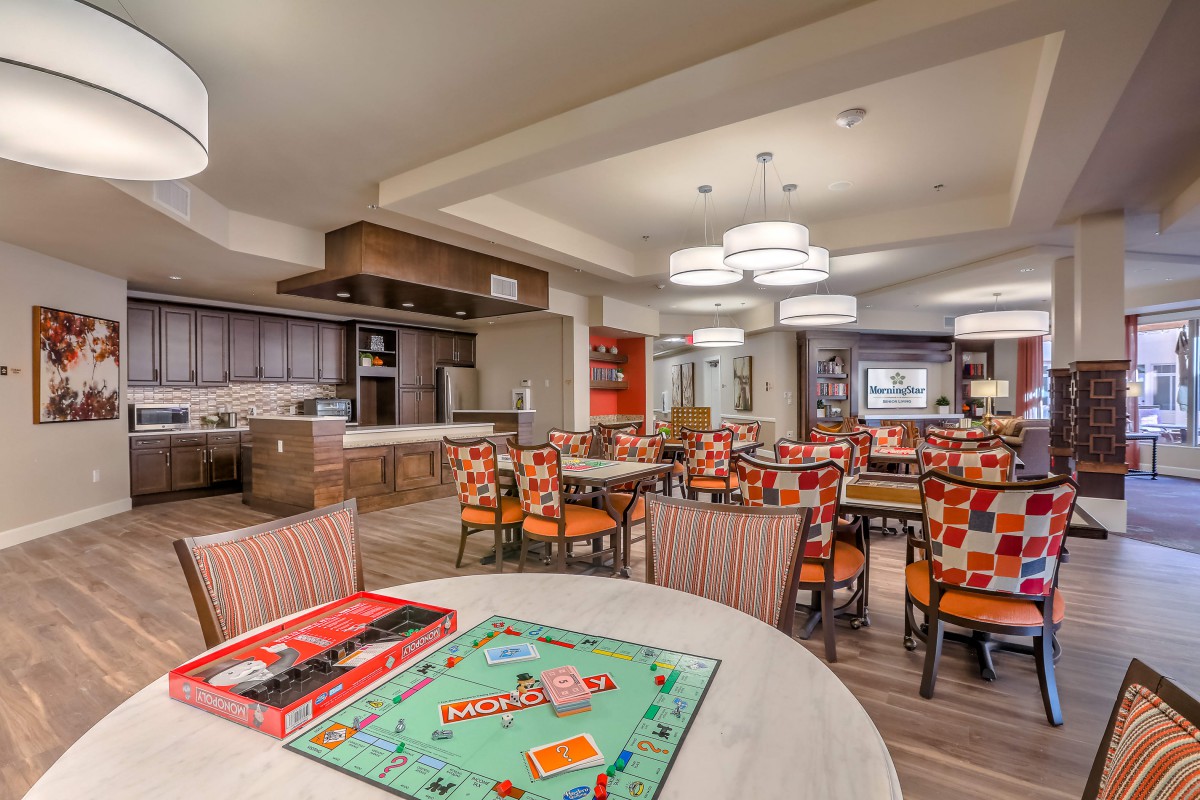 A cozy dining area with a Monopoly board game set up on a table, surrounded by colorful chairs and modern kitchen facilities.
