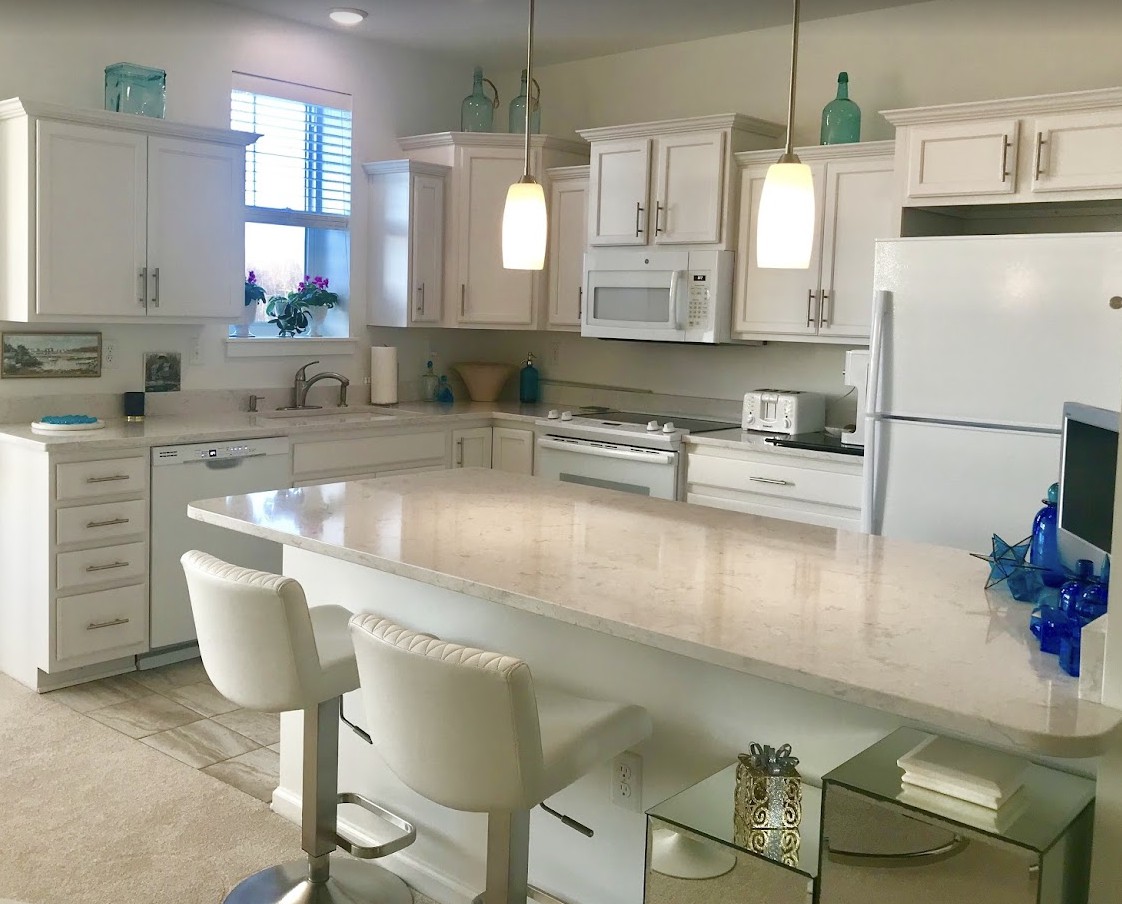 A modern kitchen with white cabinets and an island counter, featuring bar stools and pendant lights.