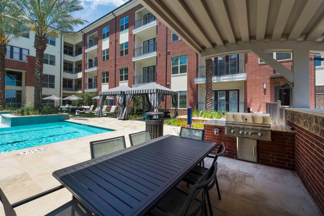 An apartment complex with a swimming pool and outdoor seating area, featuring a grill station and balconies overlooking the pool.