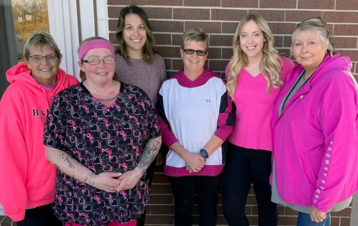 A group of women standing in front of a brick wall, smiling for the camera.