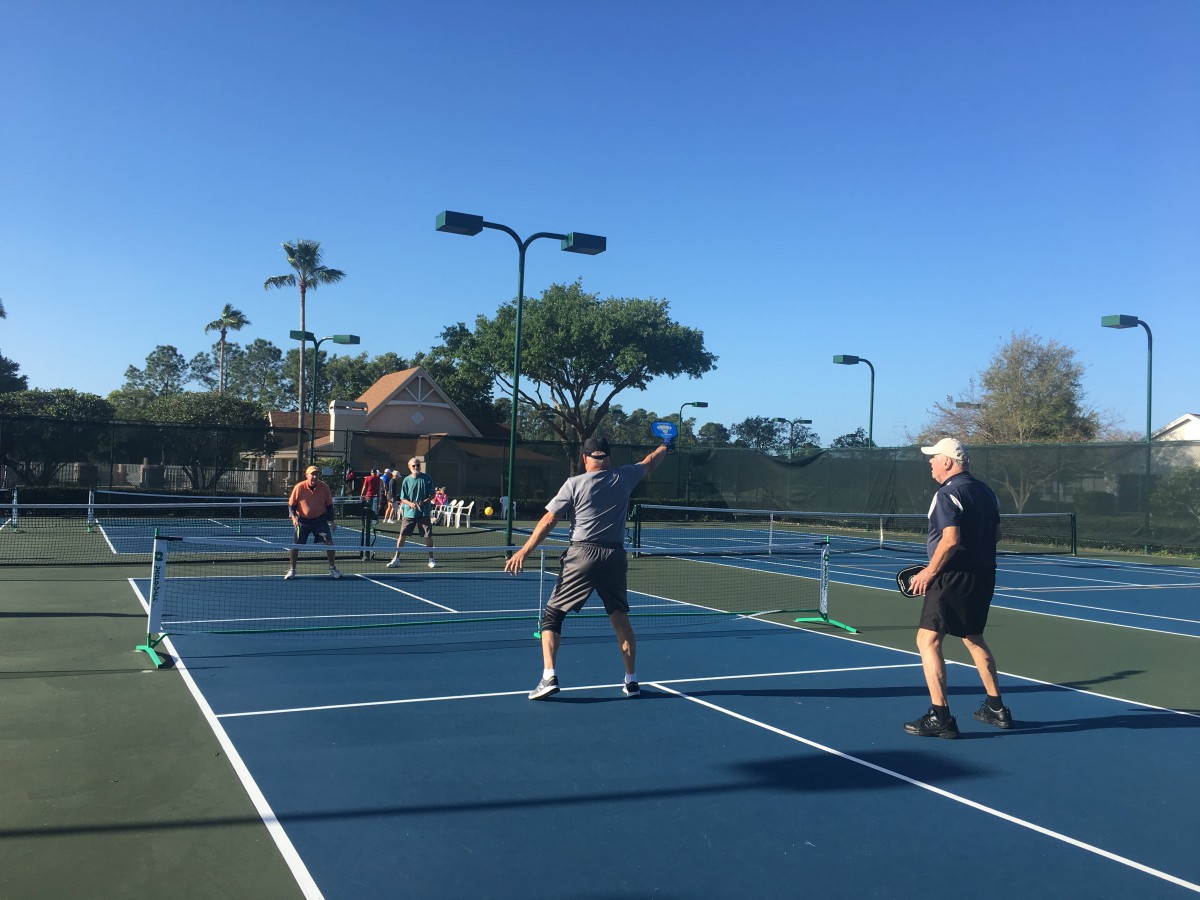 A group of people playing pickleball on a sunny day.