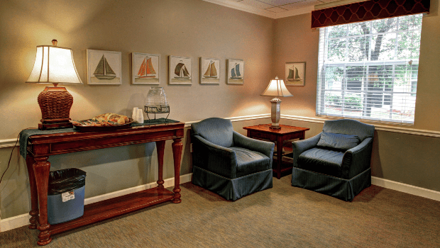 A cozy living room with two armchairs, a side table, and a lamp, adorned with decorative art on the walls.