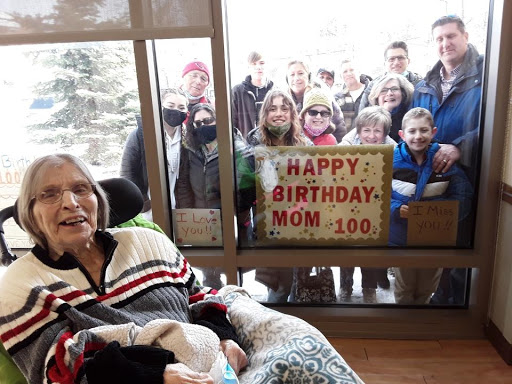 A joyful celebration of a mother's 100th birthday, with family gathered outside to send their love.