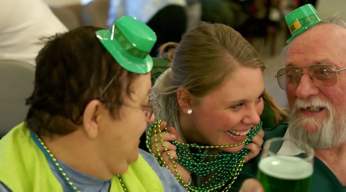 Two people enjoying a festive gathering, adorned with green hats and beaded necklaces.