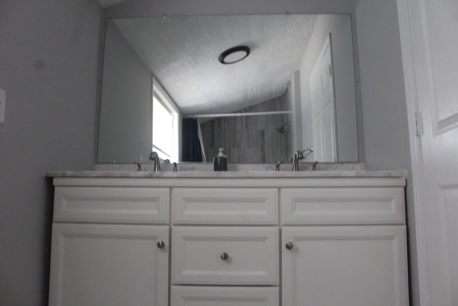 A bathroom with a large mirror above a double sink and white cabinet.