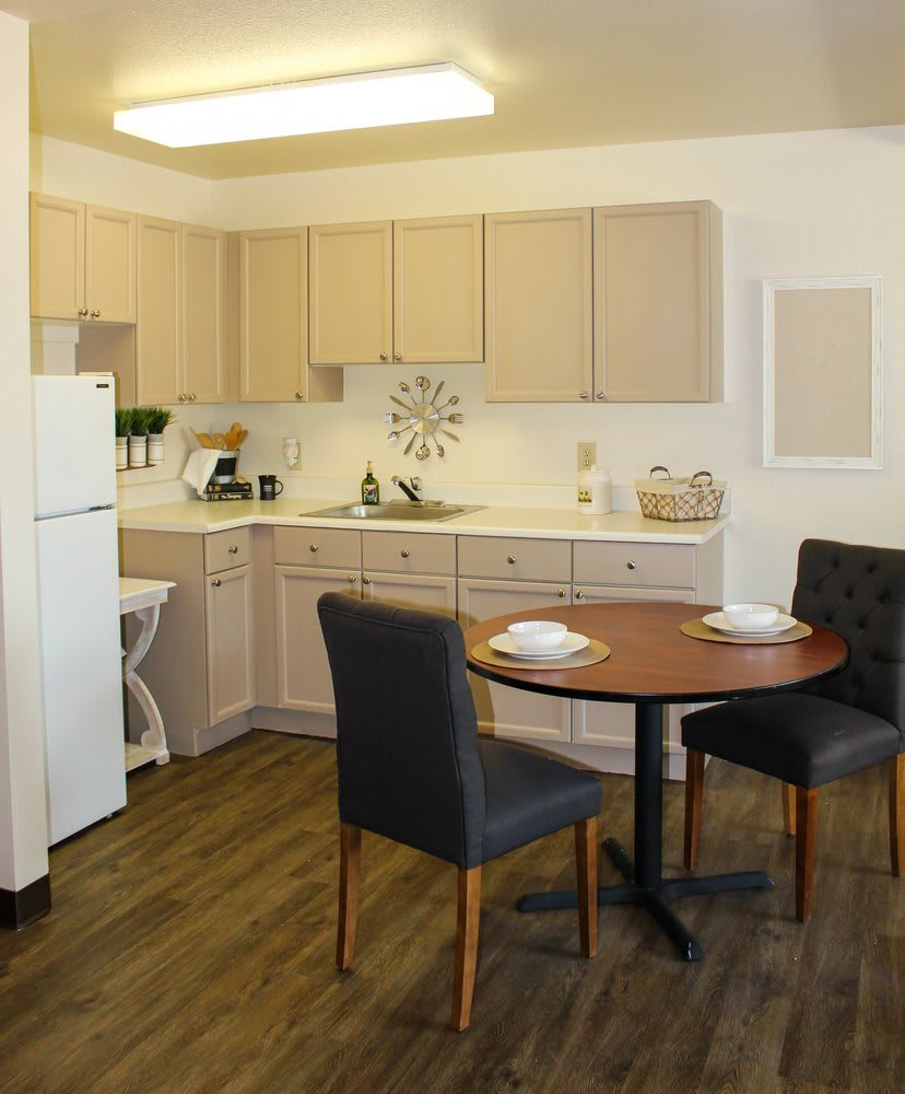 A modern kitchen with light cabinetry and a small dining area featuring two dark upholstered chairs.