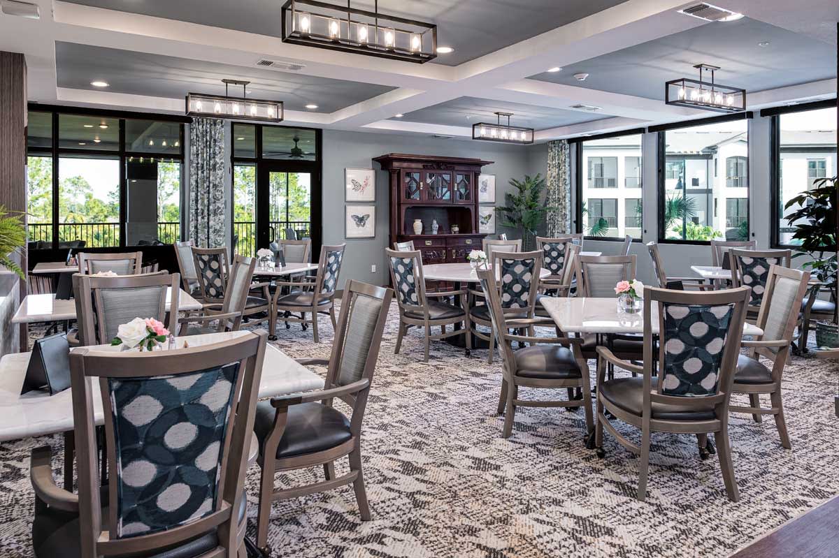 A modern dining area with elegant decor, featuring patterned chairs and tables under stylish lighting fixtures.