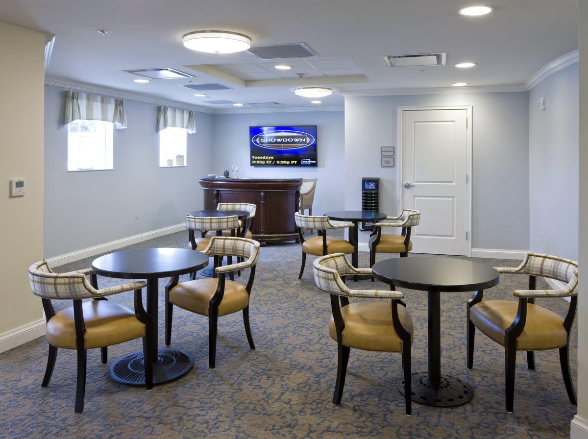 A modern meeting room with multiple tables and chairs, featuring a television on the wall.