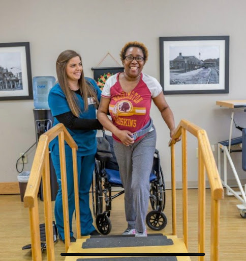A healthcare professional assists a patient as she practices walking with the help of a walking aid.