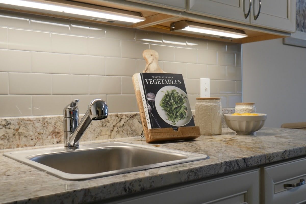 A modern kitchen countertop featuring a cookbook and under-cabinet lighting.