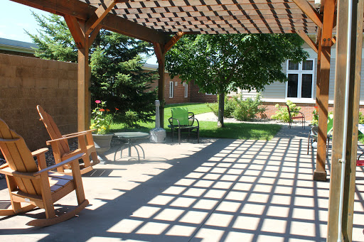A serene outdoor space with a wooden pergola casting shadows on the ground, surrounded by lush greenery.