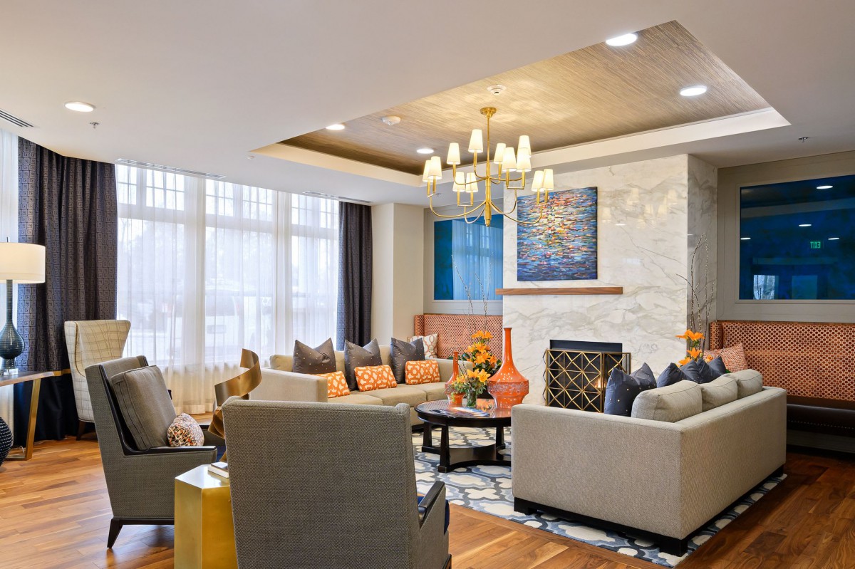 A modern living room with elegant decor, featuring comfortable sofas, a central chandelier, and contemporary artwork above a fireplace.