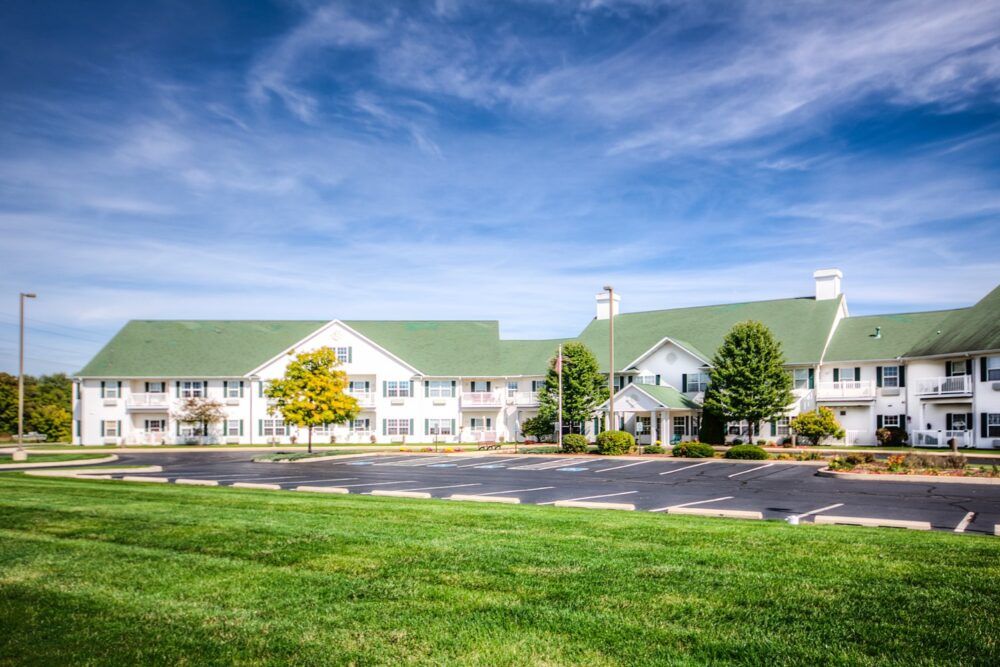 A scenic view of a large hotel with a green roof, surrounded by trees and a well-maintained lawn under a blue sky.