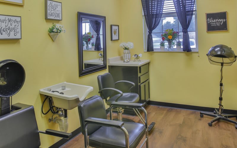 A cozy hair salon with yellow walls, featuring a mirror, sink, and salon chair.
