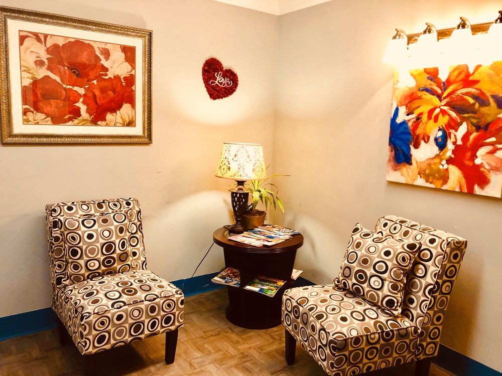 A cozy living room corner with patterned chairs, colorful artwork, and a warm lamp on a small table.