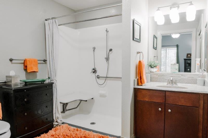 A modern, accessible bathroom with orange accents and a walk-in shower.