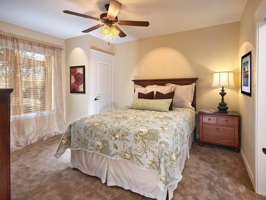 A cozy bedroom with a floral bedspread, featuring a ceiling fan and soft lighting.