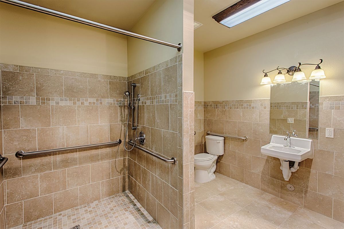 An accessible bathroom featuring a walk-in shower, toilet, and sink with grab bars.
