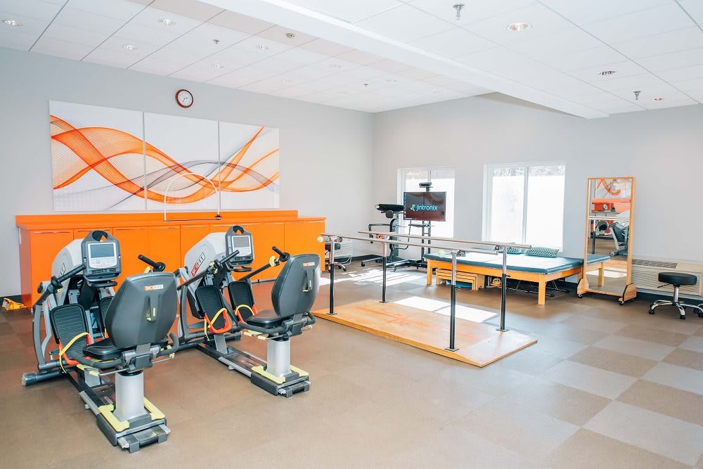 A modern fitness center with exercise equipment and a physical therapy area in a bright room.