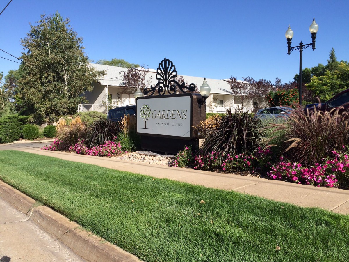 A landscaped area with a sign surrounded by grass and flowers, located near a large building.
