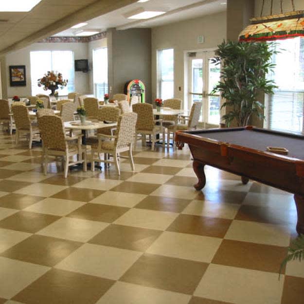 A spacious indoor area featuring a billiard table and dining tables with chairs, set on a checkered floor.