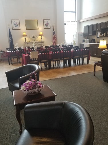 A cozy dining room with a large table, surrounded by leather chairs and decorated with flowers and lamps.