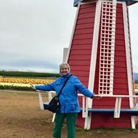 A person posing in front of a red windmill structure in an open field.