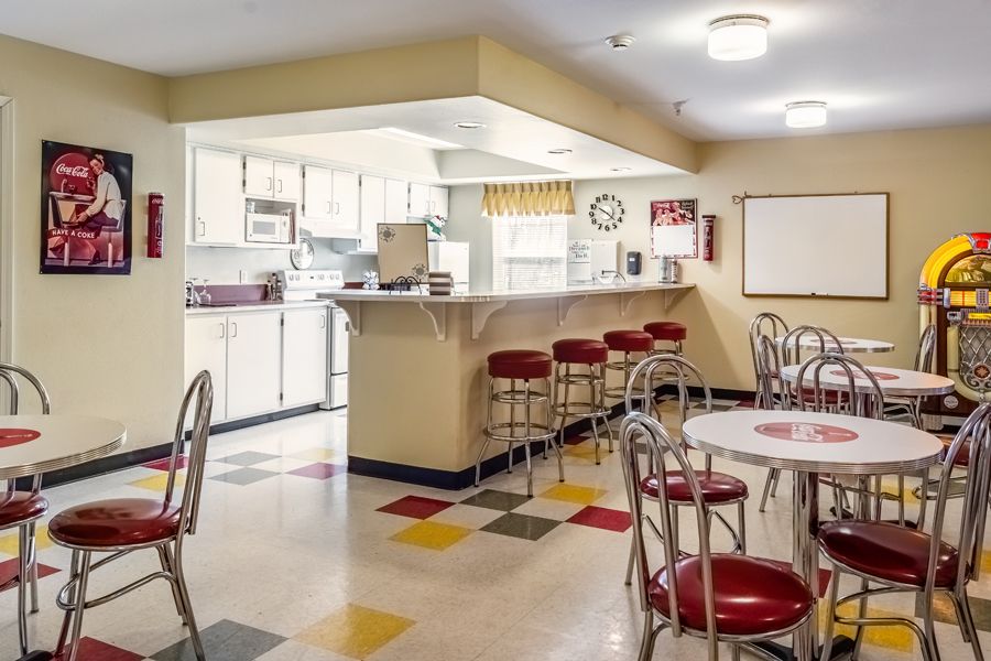 A retro-style diner kitchen with colorful flooring, counter stools, and tables.