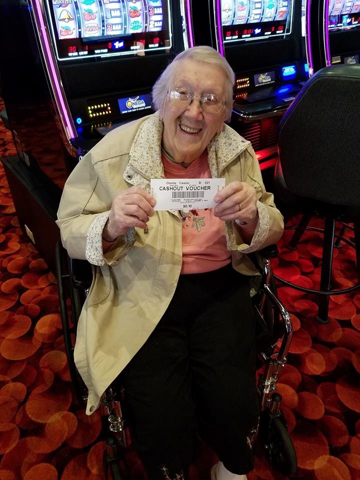 An elderly woman in a wheelchair holding a winning ticket at a casino.