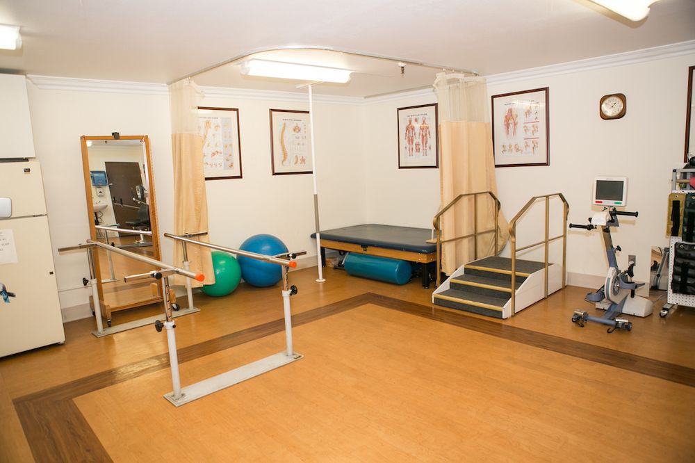 A physical therapy room equipped with parallel bars, exercise balls, and a small staircase for rehabilitation exercises.